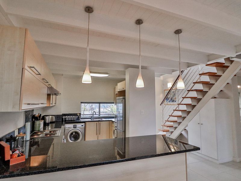 Open-plan kitchen featuring granite countertops, built-in cabinetry, integrated appliances, and a staircase leading to the upper level.