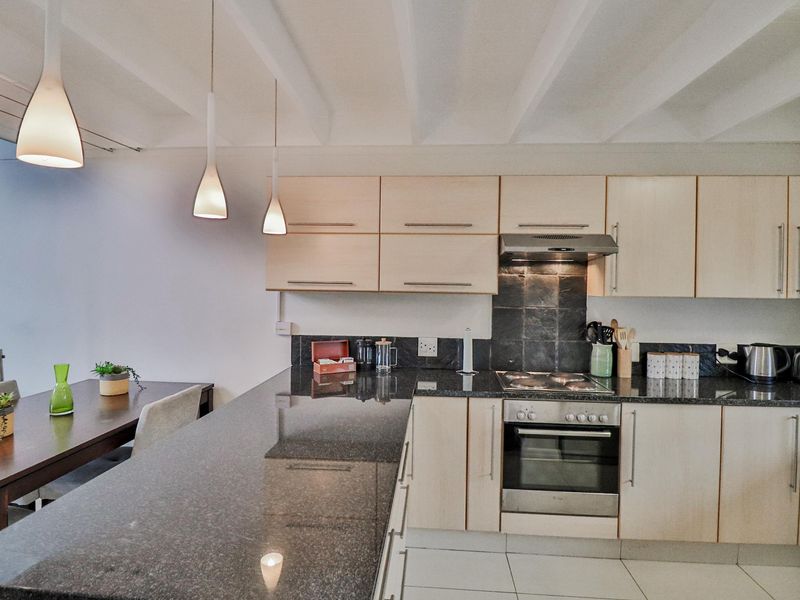 Open-plan kitchen featuring light wood cabinetry, dark granite countertops, a built-in oven, hob, and extractor fan, seamlessly flowing into the dining area.