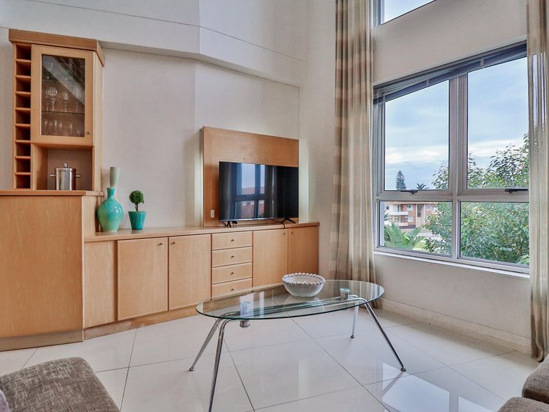 Bright living room featuring high ceilings, large windows with natural light, and custom built-in light wood cabinetry with integrated shelving.