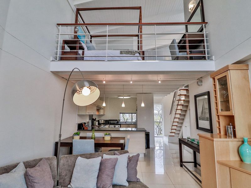 Open-plan living area featuring a modern kitchen, tiled flooring, and a mezzanine level bedroom with a sleek metal railing.