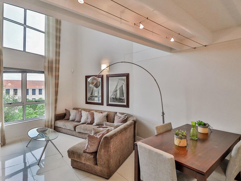 Spacious open-plan living and dining area featuring double-volume ceilings, large windows providing ample natural light, and sleek tiled flooring.