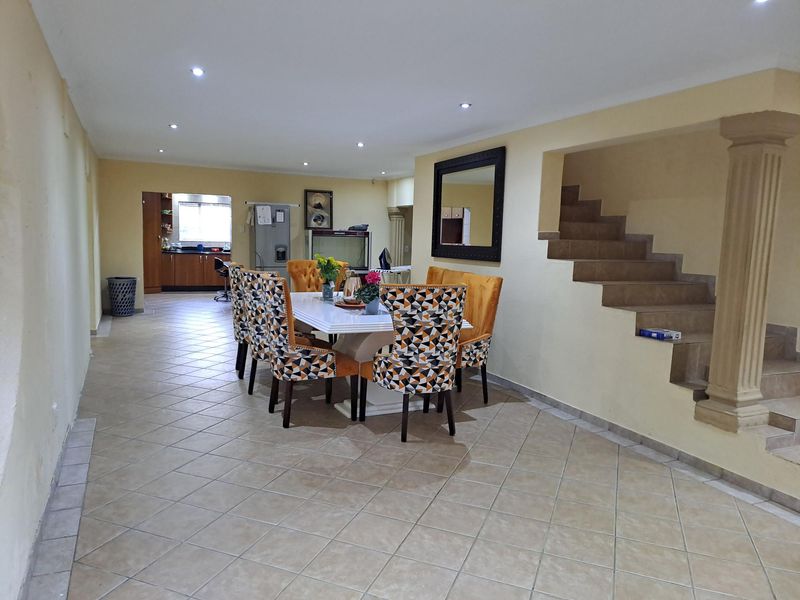 Open plan living and dining area featuring tiled flooring, recessed lighting, and a staircase with a decorative column.