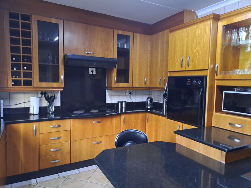 A functional kitchen featuring warm-toned wooden cabinetry, contrasting black granite countertops, built-in oven, electric hob, and integrated storage solutions.