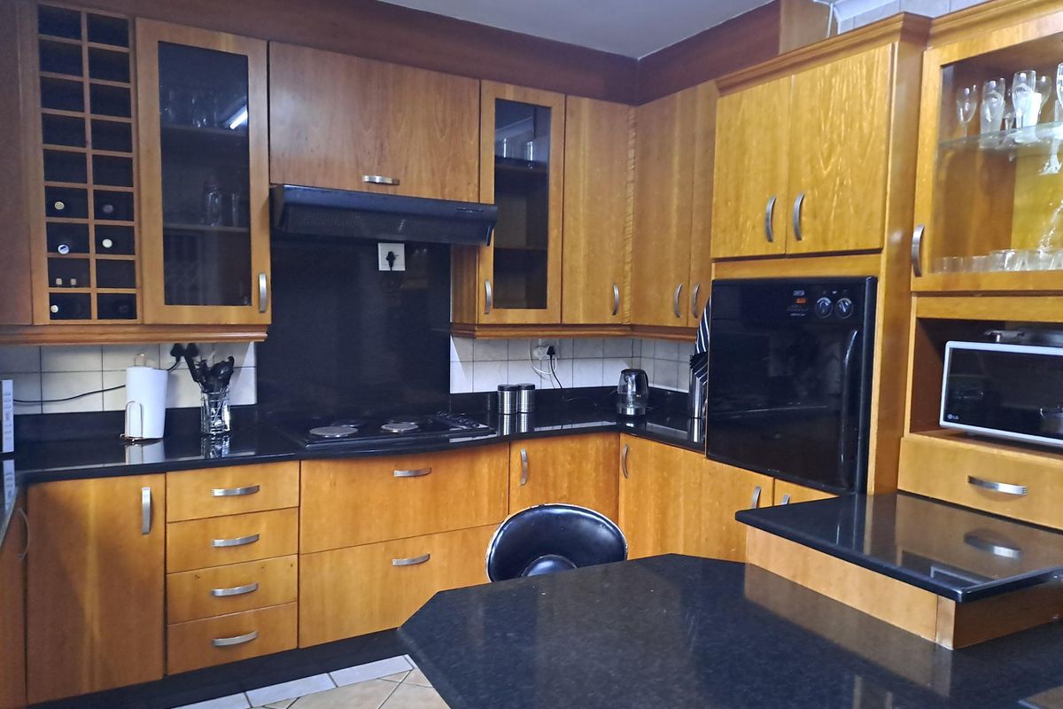 A functional kitchen featuring warm-toned wooden cabinetry, contrasting black granite countertops, built-in oven, electric hob, and integrated storage solutions.