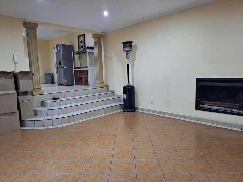 Spacious living area featuring tiled flooring, a built-in fireplace, and decorative columns leading to a raised platform area.