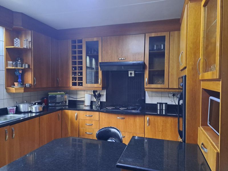 A functional kitchen featuring warm-toned wooden cabinetry, contrasting black granite countertops, and integrated appliances including an oven and hob.