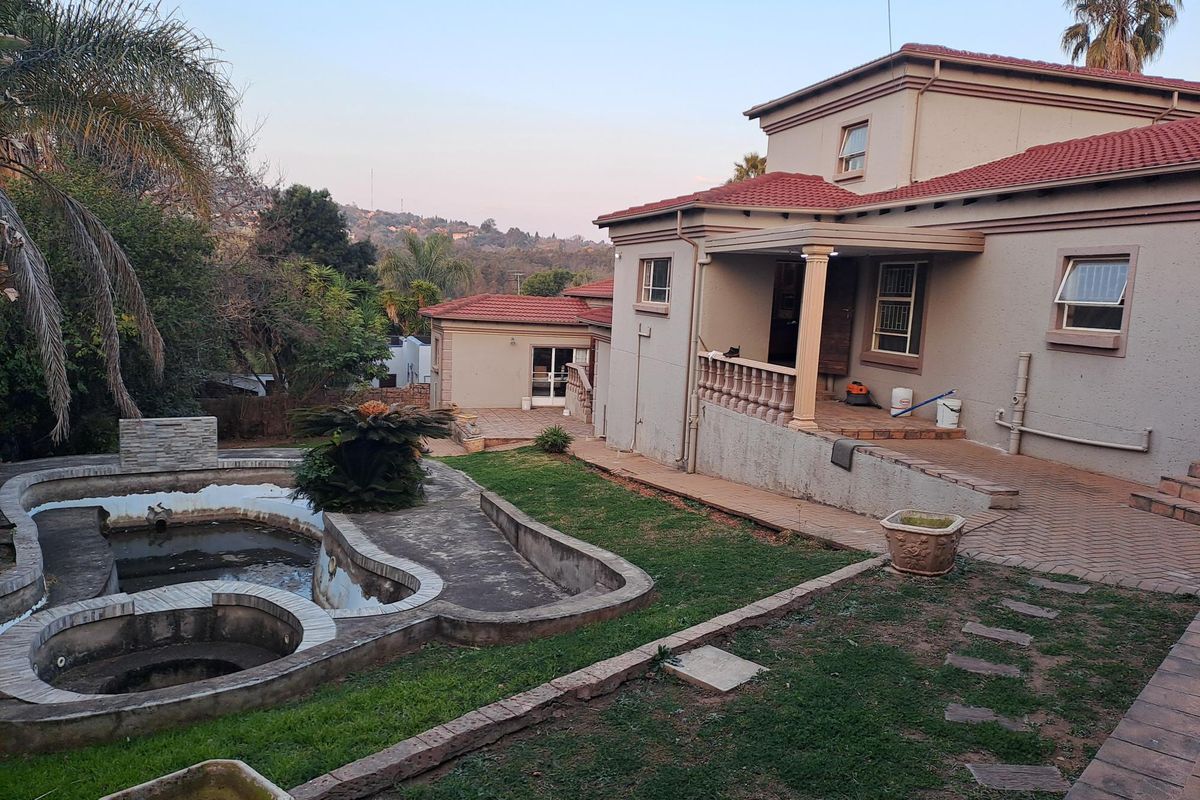 Rear view of the property featuring a multi-level swimming pool, paved patio area, and established garden with terracotta roof tiles.