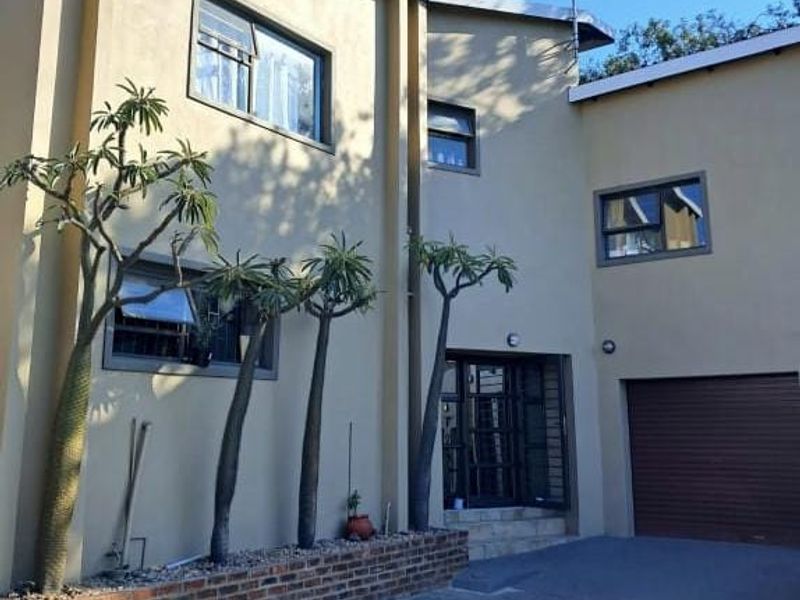 Front elevation of a modern double-storey house featuring a paved driveway, integrated garage, and a brick-lined planter bed with established trees.