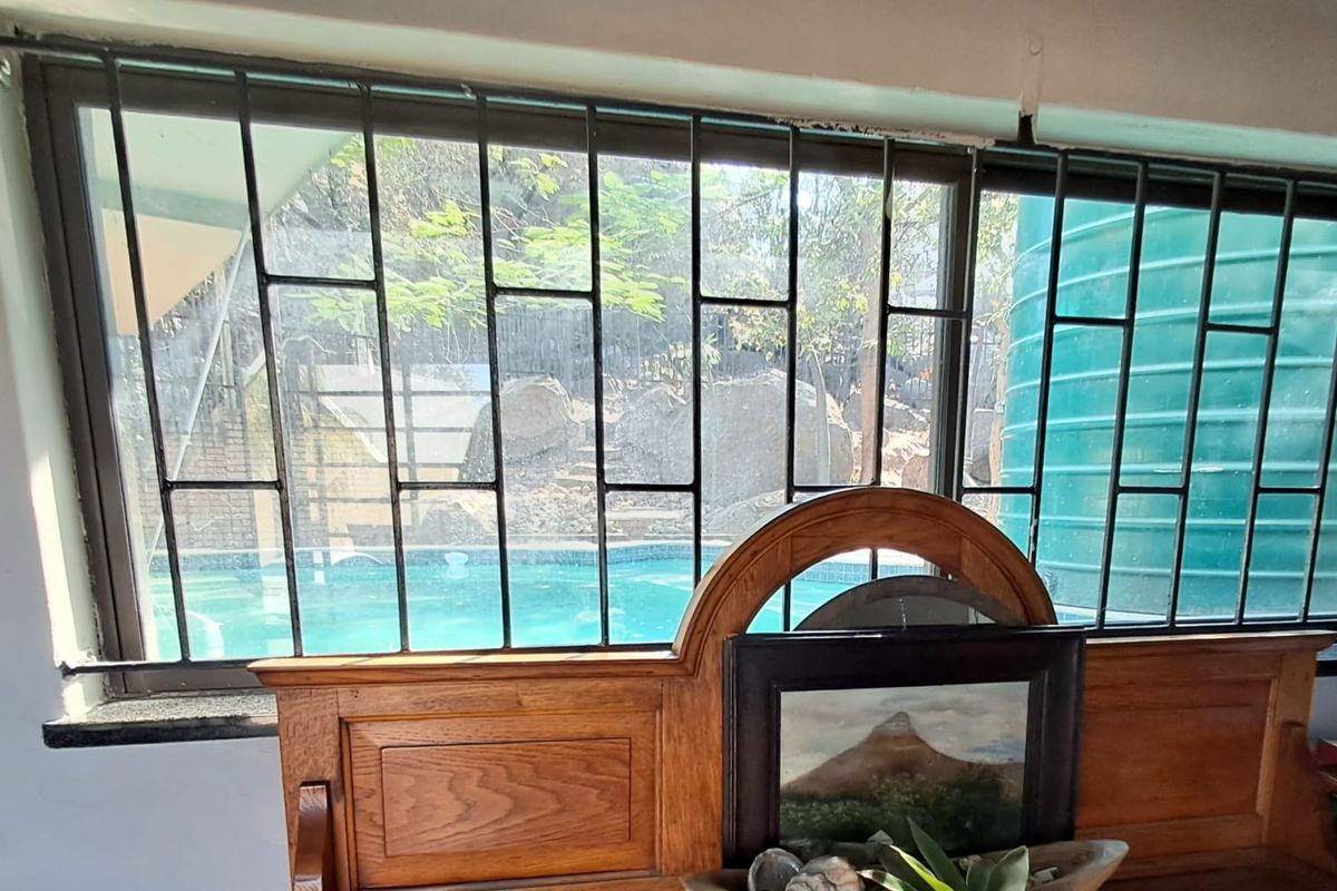 Interior view looking through a window with security bars, featuring a view of the outdoor swimming pool area.