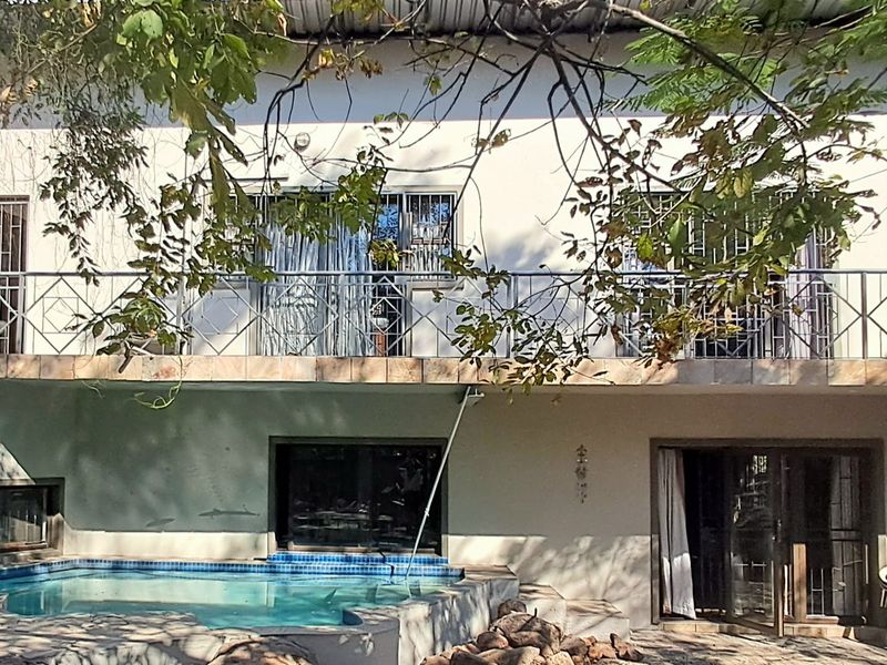 Rear elevation featuring a swimming pool, paved patio area, and an upper-level balcony with metal railings.