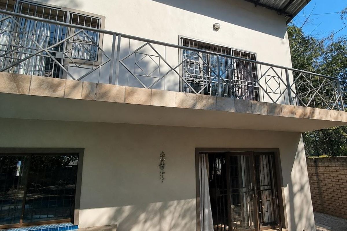 Rear view of the house featuring a spacious upper-level balcony with metal railings, sliding glass doors, and access to the ground-level pool area.