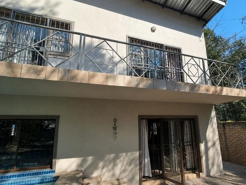 Rear view of the house featuring a spacious upper-level balcony with metal railings, sliding glass doors, and access to the ground-level pool area.