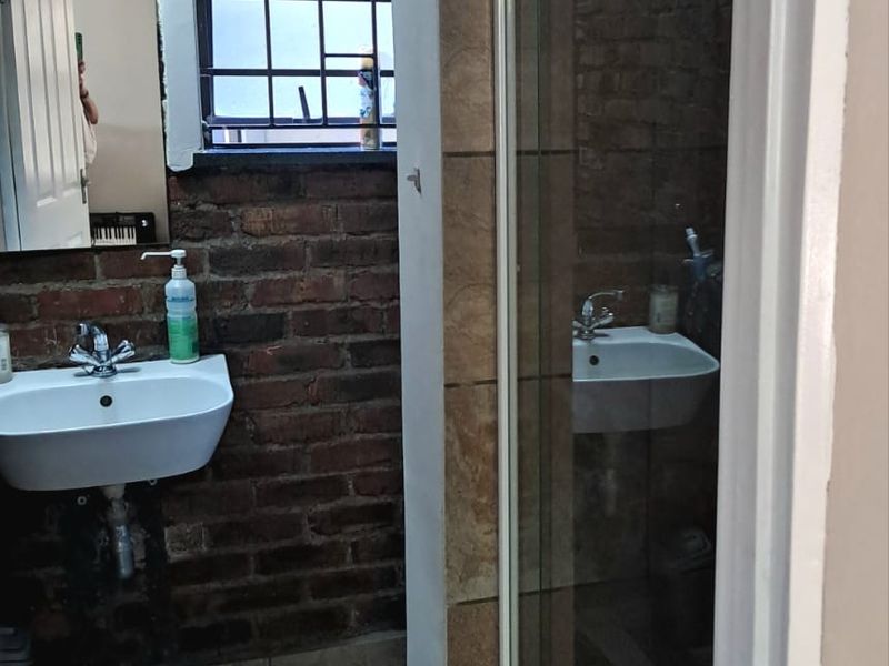 A compact bathroom featuring exposed brick walls, ceramic floor tiling, a wall-mounted basin, and a glass-enclosed shower unit.