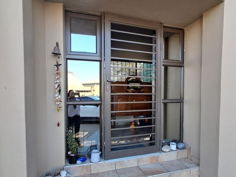 Front entrance featuring a secure metal gate, aluminium window frames, and a tiled step leading into the home.