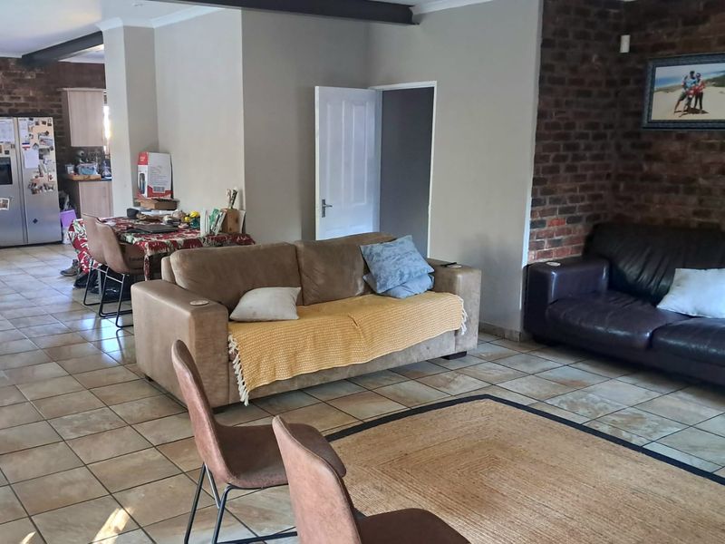 Spacious open-plan living area featuring ceramic floor tiles, an exposed brick feature wall, and an exposed ceiling beam, connecting to the kitchen area.