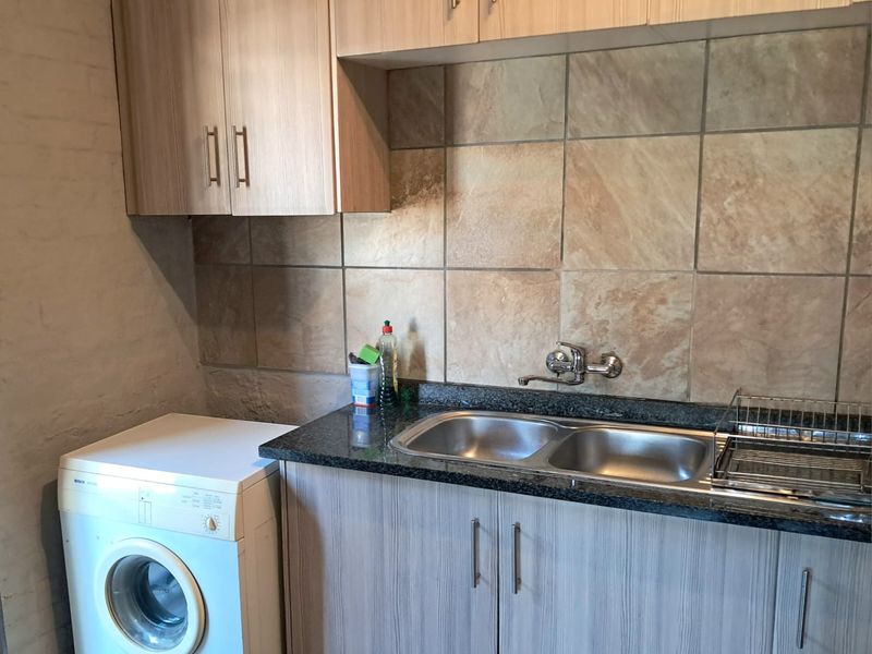 A functional laundry area featuring built-in cabinetry, a granite countertop, and a double stainless steel sink with tiled splashback.