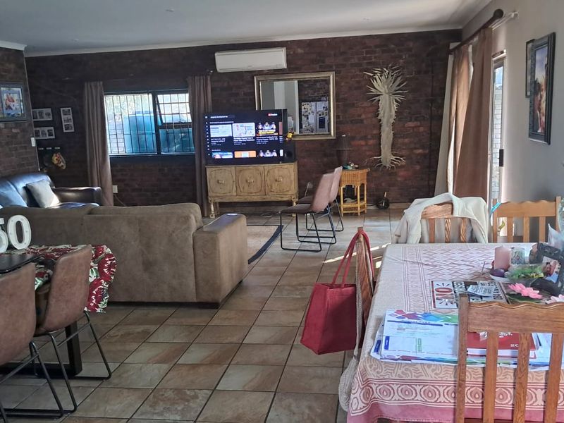 Spacious open-plan living and dining area featuring exposed brick walls, tiled flooring, and a wall-mounted air conditioning unit.
