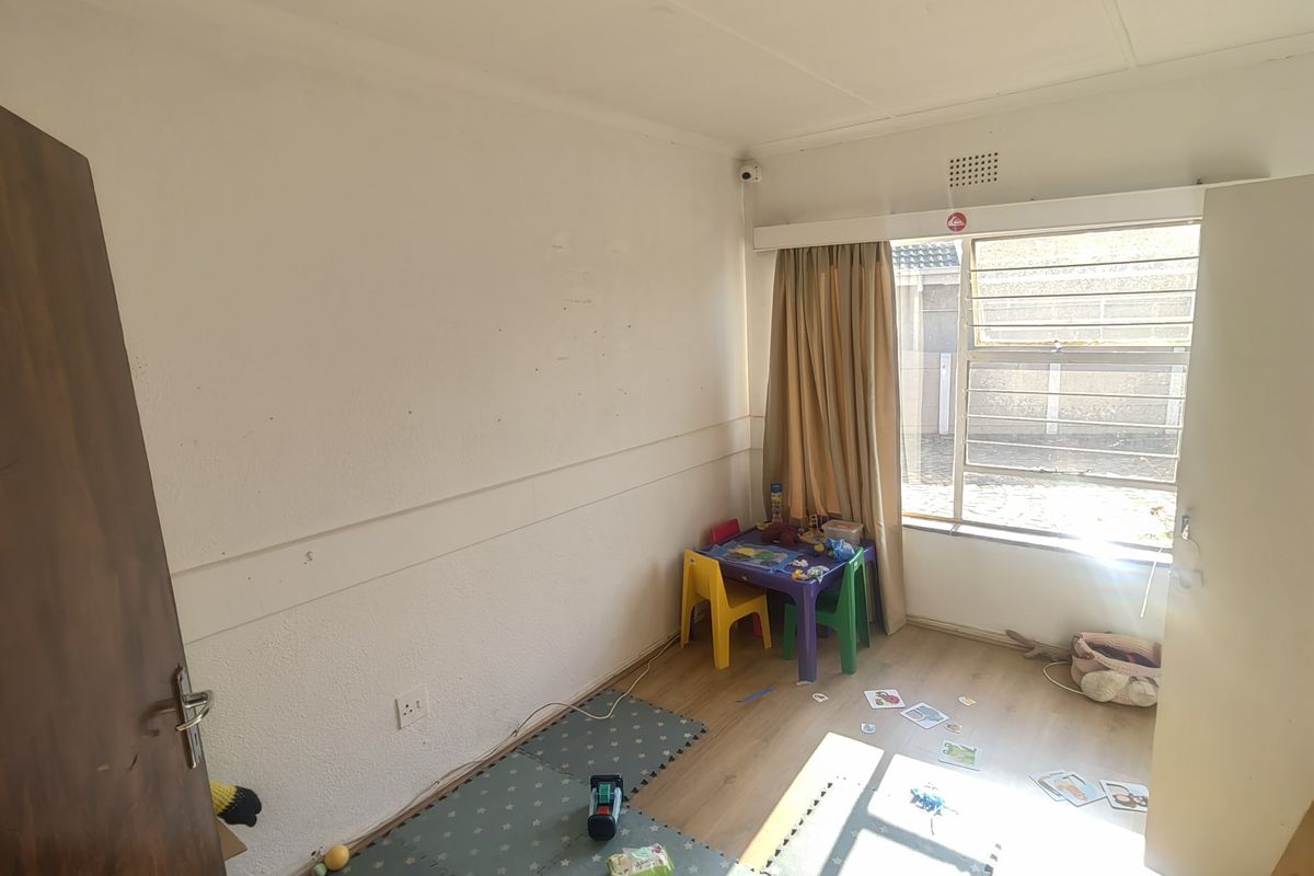 A bedroom featuring laminate flooring and an aluminium window with security bars, requiring minor cosmetic updates to the walls.