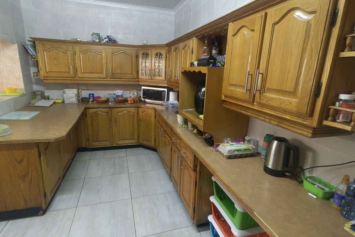 A functional kitchen featuring traditional wood-finish cabinetry, ample laminate countertop workspace, and tiled flooring with a neutral tiled backsplash.