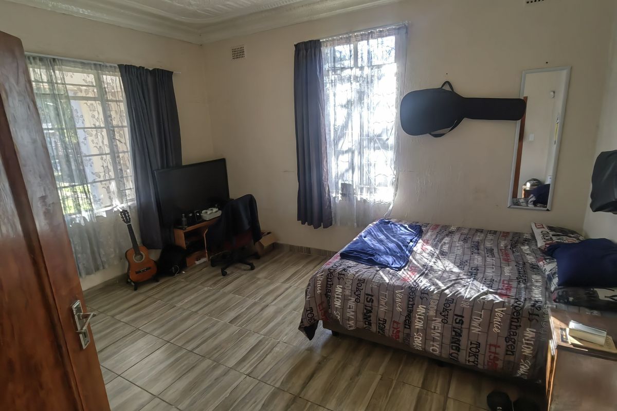 A bedroom featuring tiled flooring and a classic pressed metal ceiling, offering a functional space with natural light from two large windows.