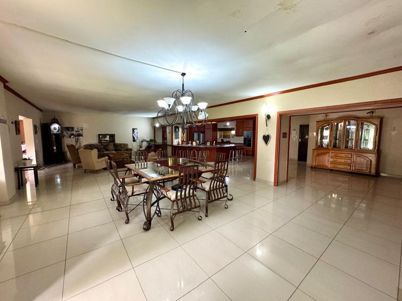 Spacious open-plan living and dining area featuring large format floor tiles, a central chandelier, and an integrated kitchen layout.