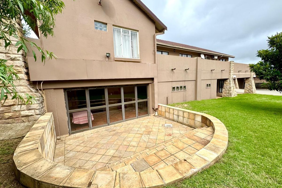 Rear view of the property featuring a paved patio area, large glass sliding doors, and a spacious lawn with stone masonry accents.