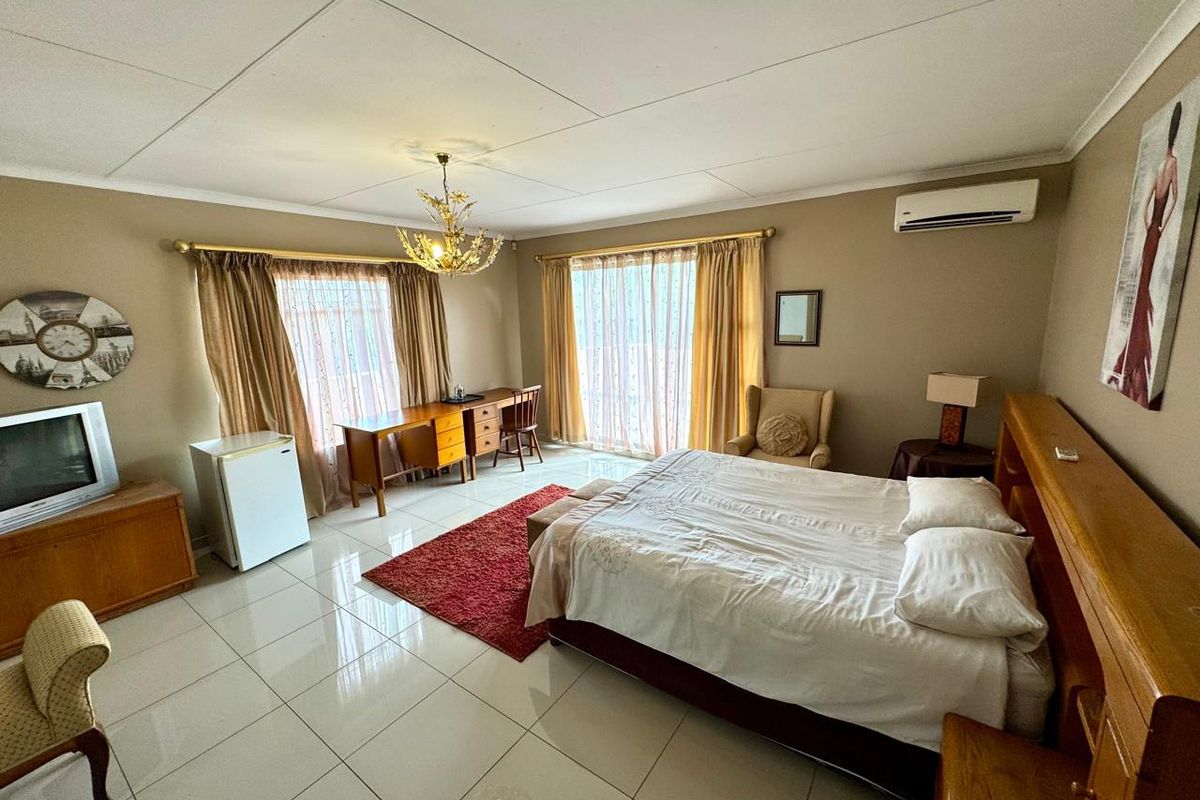 Spacious bedroom featuring tiled flooring, a wall-mounted air conditioning unit, and large windows with curtain tracks.