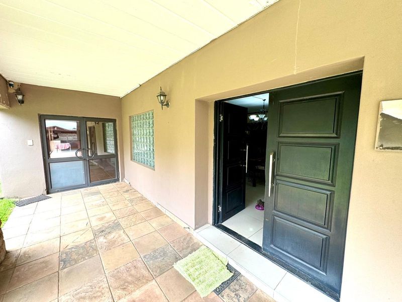 Covered entrance patio featuring tiled flooring, glass block window detail, and a double door entry leading into the home.