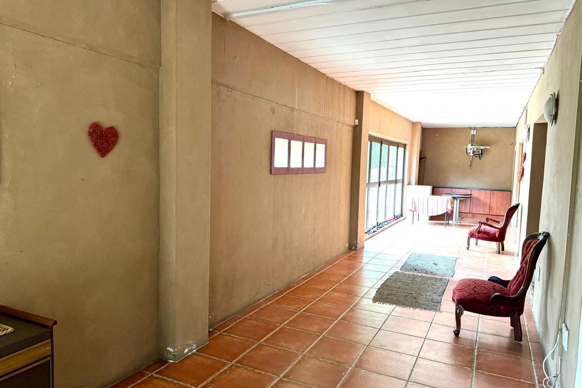 A spacious, elongated living area featuring terracotta floor tiles, large windows providing natural light, and a neutral wall finish.