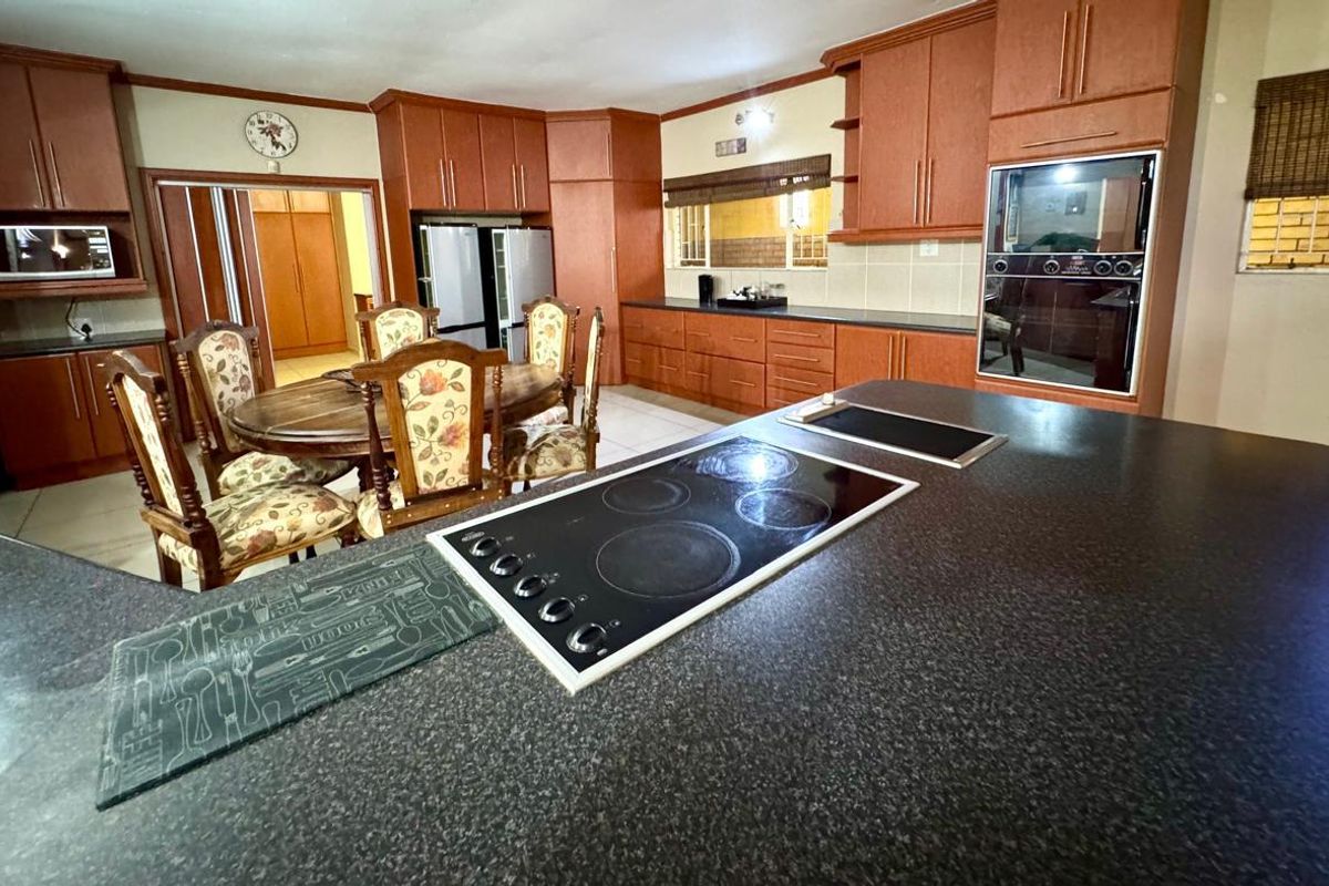 Spacious kitchen featuring dark laminate countertops, built-in cabinetry, integrated oven, and a central island with a built-in electric hob.