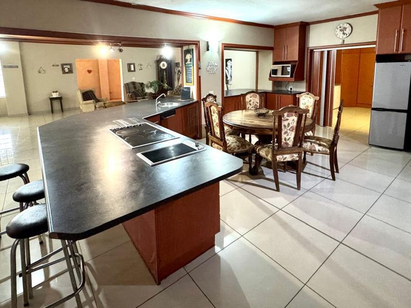 Spacious open-plan kitchen and dining area featuring a large breakfast bar, built-in cabinetry, and tiled flooring throughout.