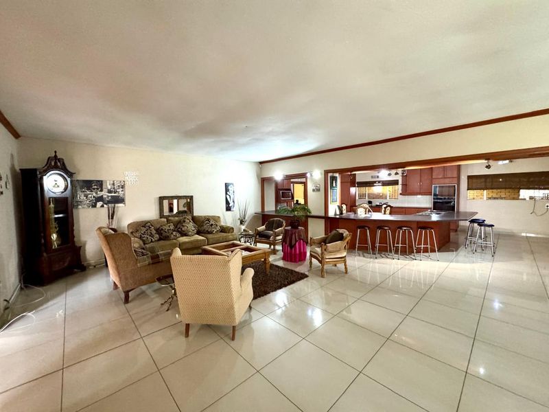 Spacious open-plan living area featuring large format floor tiles, a breakfast bar, and a functional kitchen with built-in oven and cabinetry.