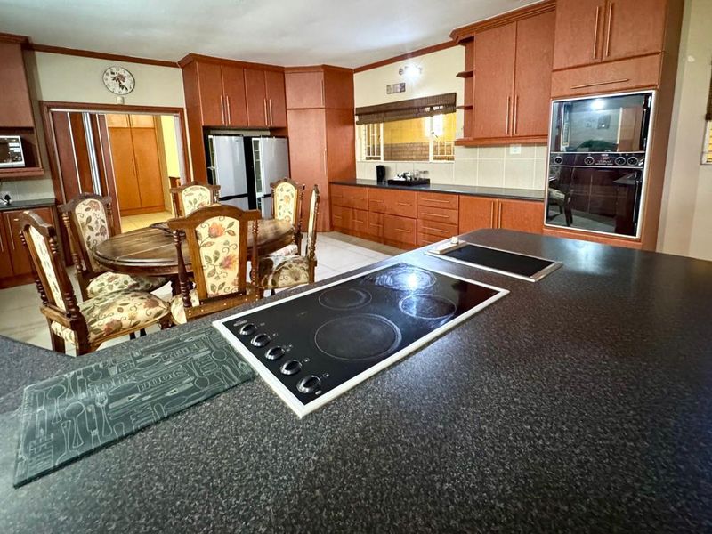 Spacious kitchen featuring dark laminate countertops, built-in cabinetry, integrated oven, and a central island with a built-in electric hob.