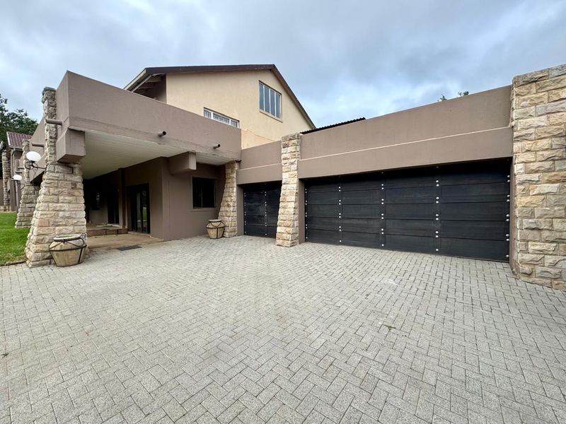 Front exterior view of the property featuring a paved driveway, double garage with dark panelled doors, and decorative stone pillar accents.