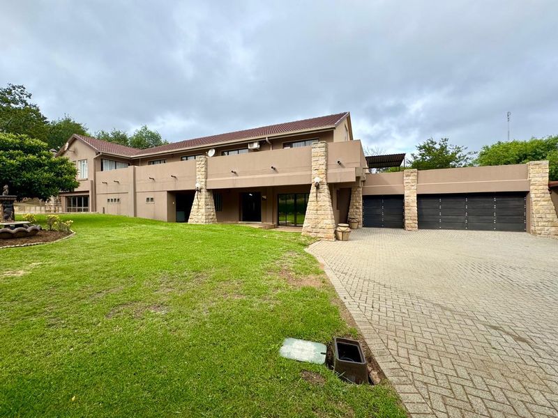 Spacious exterior view of the property featuring a paved driveway, double garage, stone-clad pillars, and a well-maintained lawn.