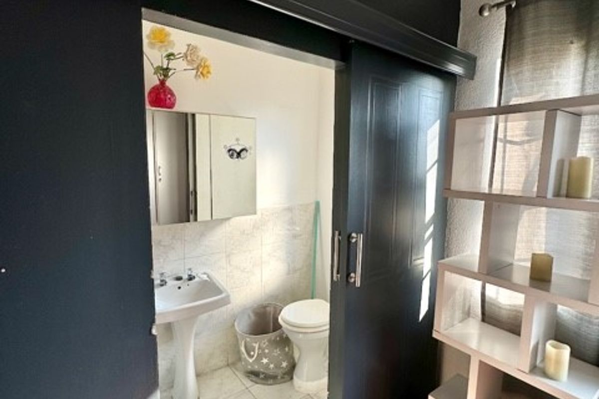 A bathroom featuring a pedestal basin and toilet, accessed via a dark-painted sliding barn door from an adjacent room with wooden flooring.