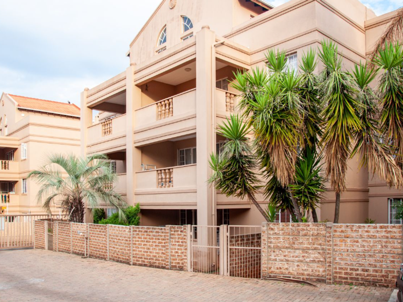 Exterior view of a multi-story townhouse complex featuring private balconies with balustrades, brick boundary walls, and paved driveway access.