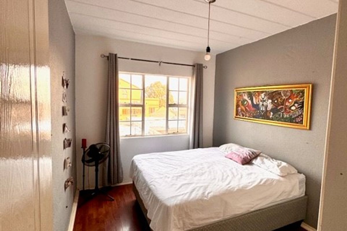 A bedroom featuring dark wood-look flooring, a large window providing natural light, and a simple pendant light fixture.