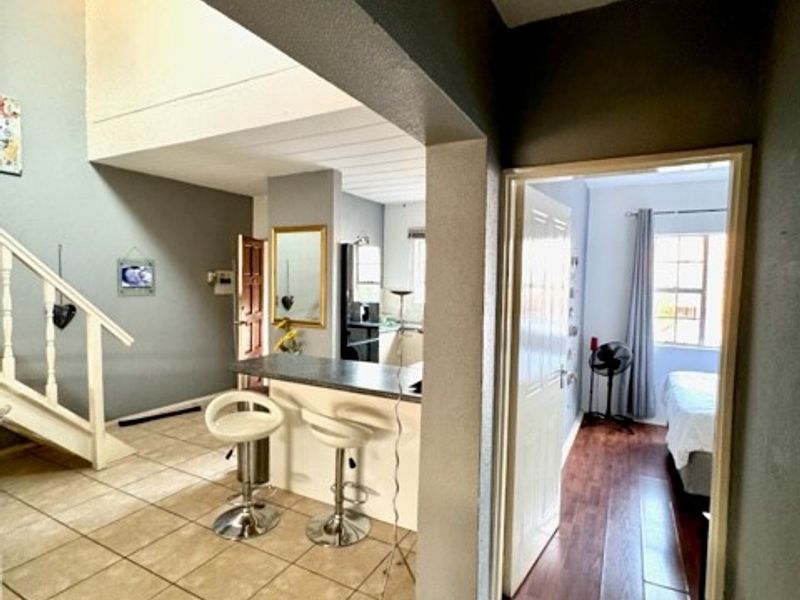 Open plan living area featuring a breakfast bar, tiled flooring, and a staircase, with an adjacent bedroom accessible through a doorway.