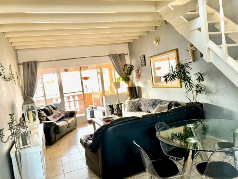 Open plan living and dining area featuring exposed ceiling beams, tiled flooring, and a staircase leading to the upper level.
