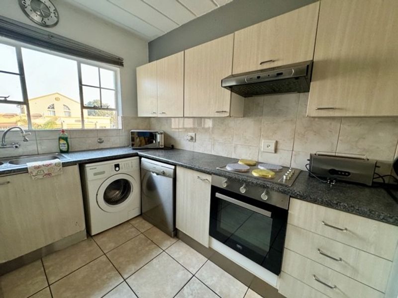 Functional kitchen featuring light wood-tone cabinetry, granite-look countertops, built-in oven, electric hob, extractor fan, and integrated space for laundry and dishwasher appliances.
