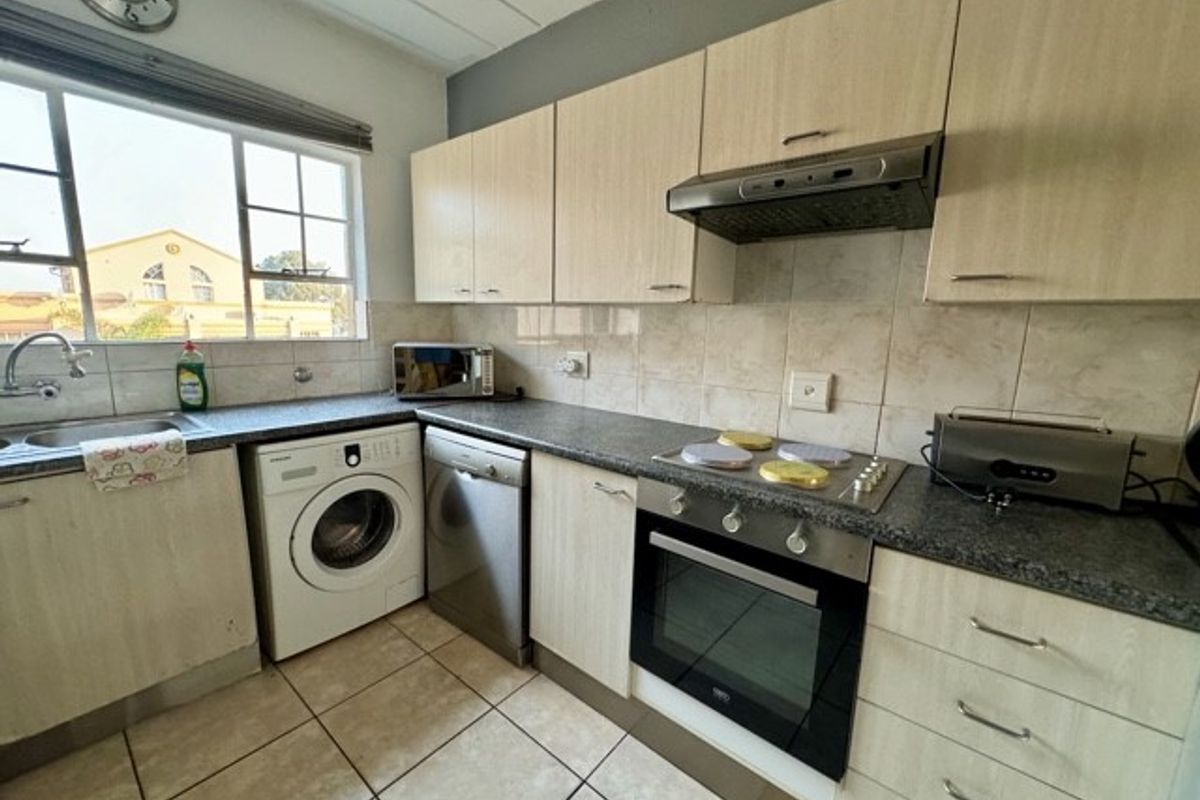 Functional kitchen featuring light wood-tone cabinetry, granite-look countertops, built-in oven, electric hob, extractor fan, and integrated space for laundry and dishwasher appliances.