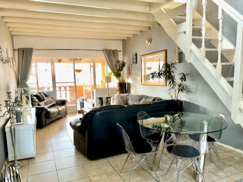 Open plan living and dining area featuring exposed ceiling beams, tiled flooring, and a staircase leading to the upper level with access to a patio.