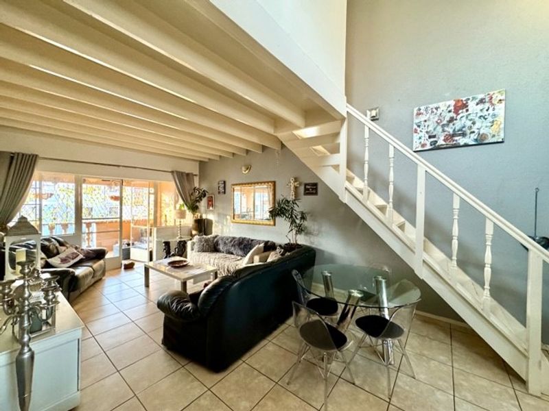 Open-plan living and dining area featuring high ceilings with exposed beams, a staircase, and direct access to an outdoor patio space.