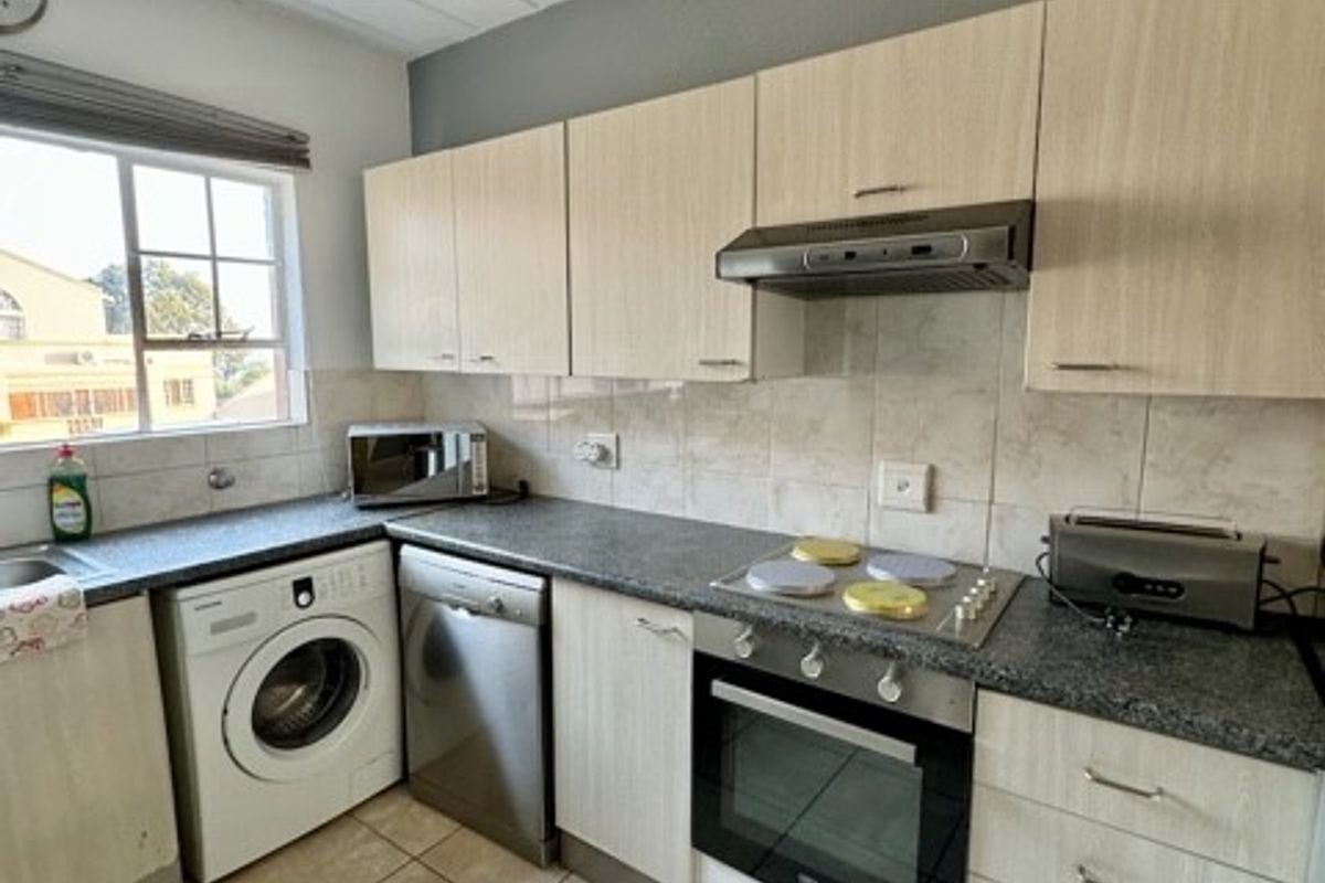 Functional kitchen featuring light wood-look cabinetry, granite-style countertops, built-in oven, hob, extractor fan, and integrated space for laundry appliances.
