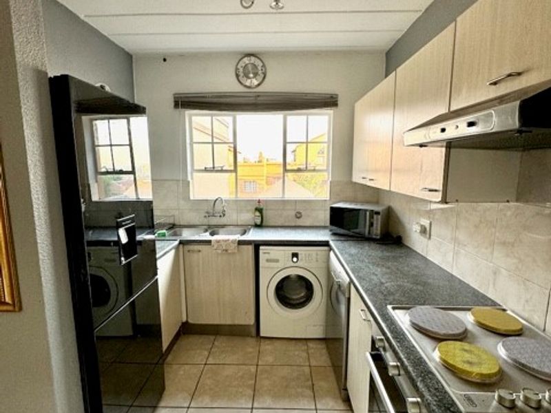 A functional galley-style kitchen featuring built-in cabinetry, a fitted oven and hob, extractor fan, and integrated space for laundry appliances.
