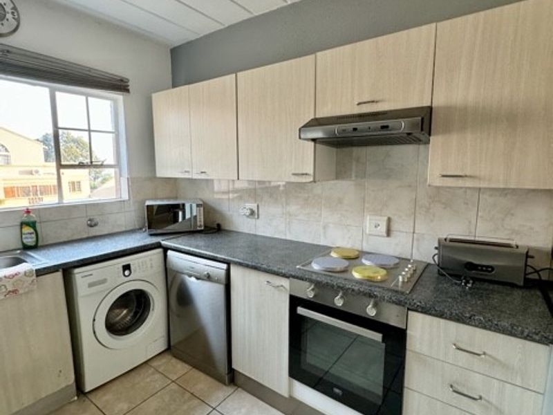 Functional kitchen featuring light wood-look cabinetry, granite-style countertops, built-in oven, hob, extractor fan, and integrated space for laundry appliances.