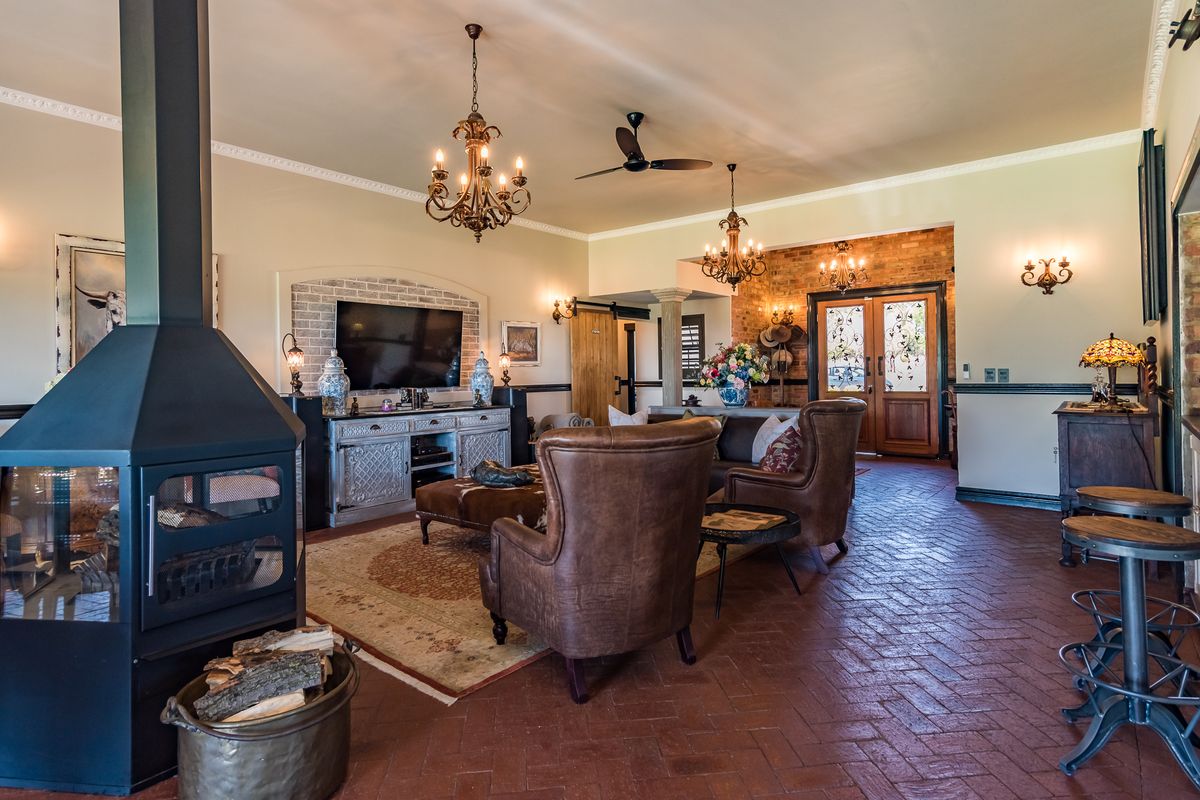 Spacious living area featuring a prominent freestanding fireplace, terracotta tile flooring, exposed brick accents, and elegant chandeliers, creating a warm and inviting atmosphere.