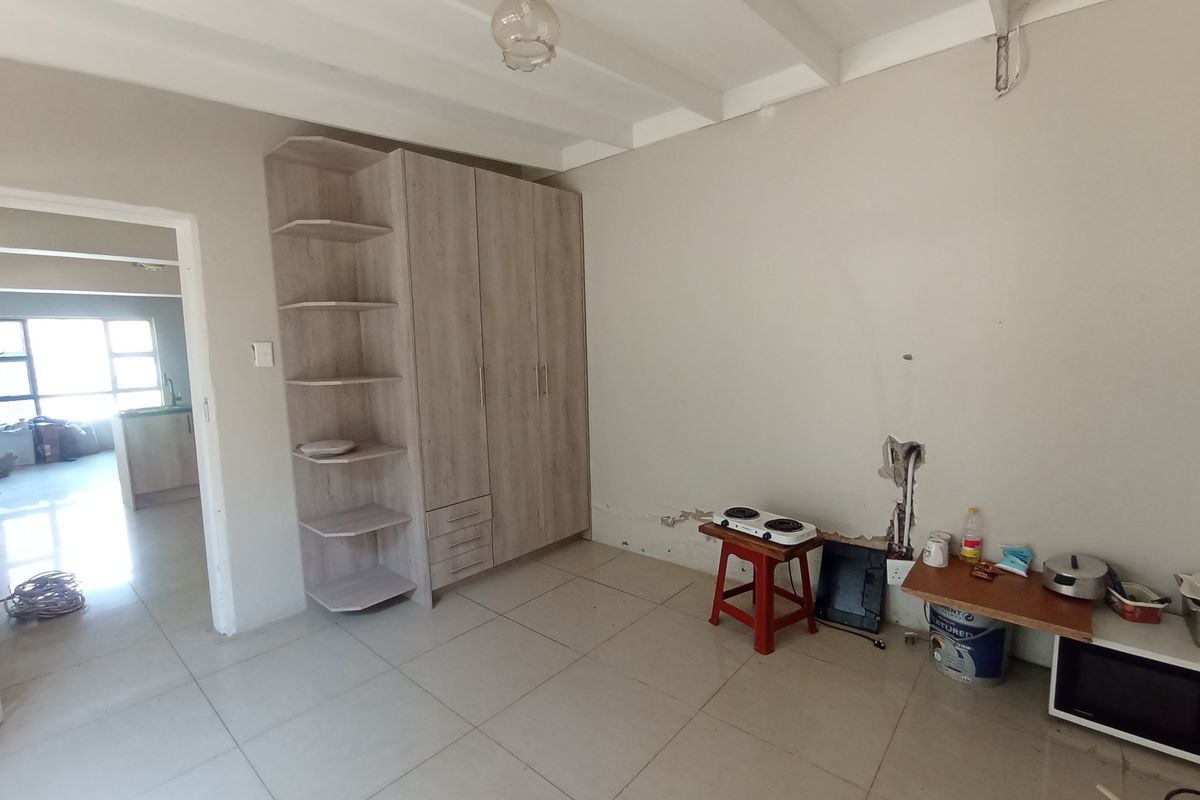 A bedroom featuring built-in cabinetry, tiled flooring, and exposed beam ceilings, currently requiring wall repairs and cosmetic updates.