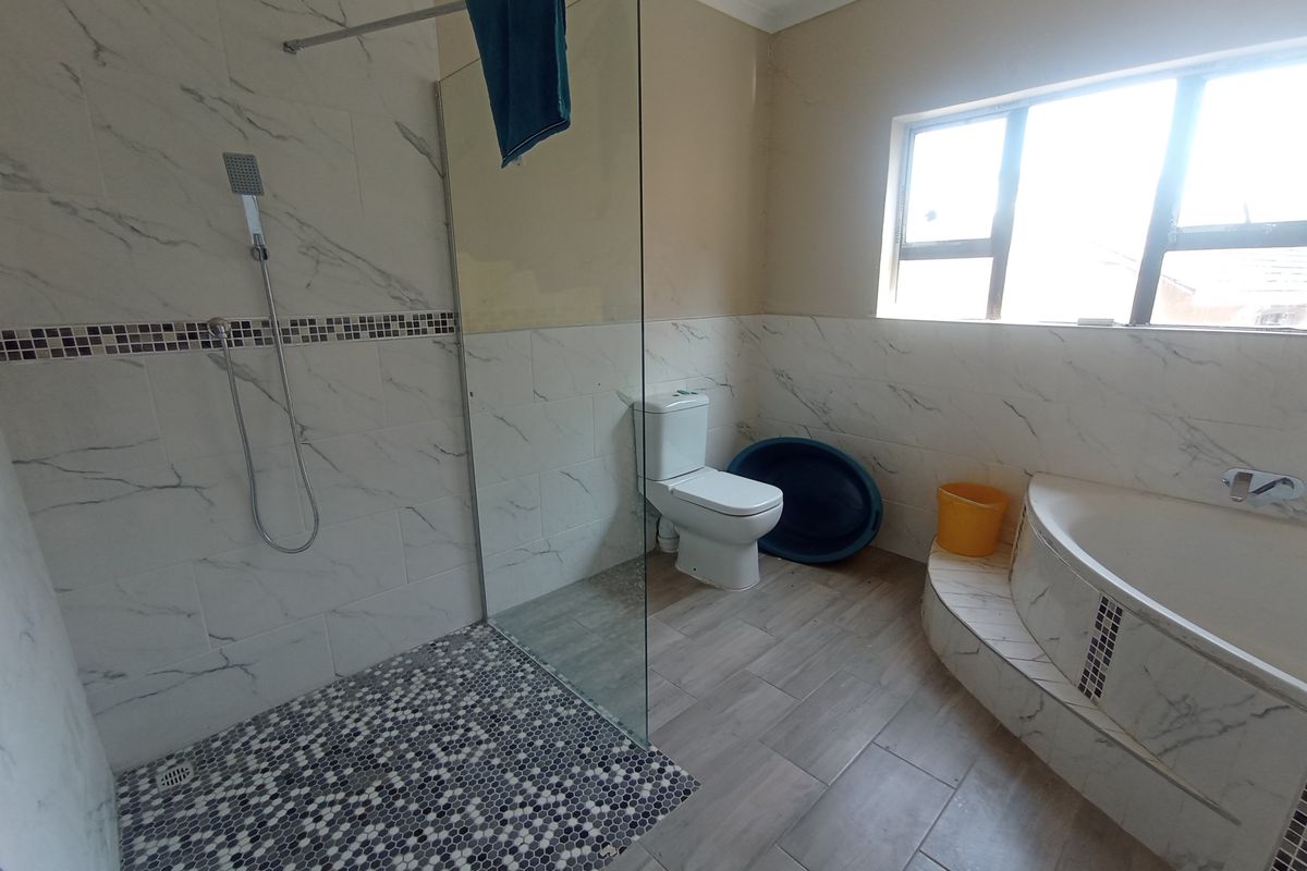 A spacious bathroom featuring a walk-in shower with glass screen, a built-in bathtub, and a toilet, finished with marble-look wall tiles and wood-look floor tiles.